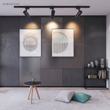 Three black track spotlights above framed prints in a lounge