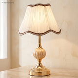Warm-lit gold glass table lamp beside a green plant and teacup