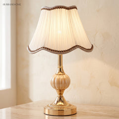 Warm-lit gold glass table lamp beside a green plant and teacup