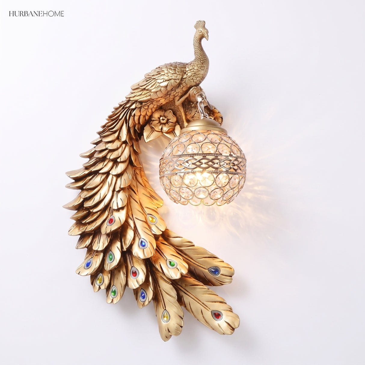 Gold peacock wall sconce with jewel-accented tail feathers on a white background