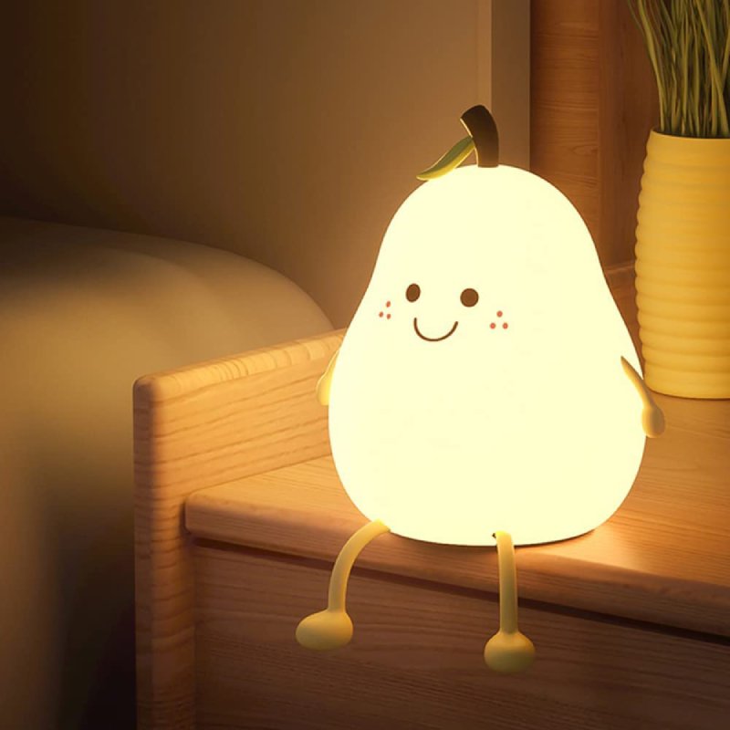 Smiling pear silicone night light glowing warm on a wooden nightstand