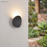 Pebble outdoor wall light on a rendered wall beside a garden path