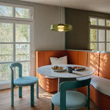Green glass pendant light over a marble table beside an orange banquette