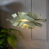 Sage green petal pendant light lit by a panelled wall and fern