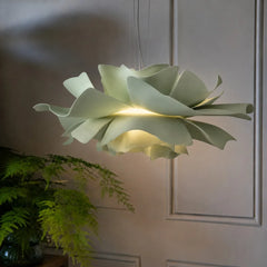 Sage green petal pendant light lit by a panelled wall and fern