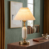 White pleated-shade table lamp with brass base on a wood sideboard