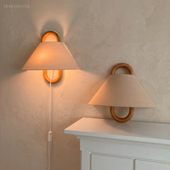 Pleated fabric wall sconce with beechwood mount glowing softly on a wall
