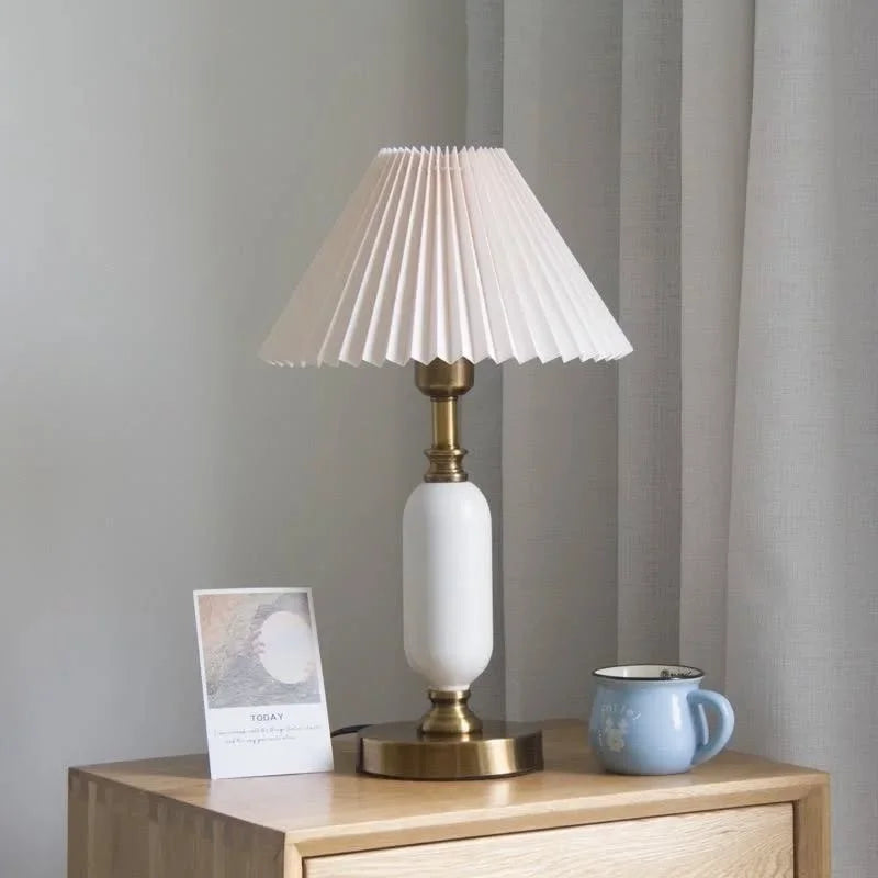 White pleated table lamp with brass base, angled view