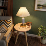 White pleated table lamp on a round side table by a green wall