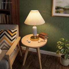 White pleated table lamp on a round side table by a green wall