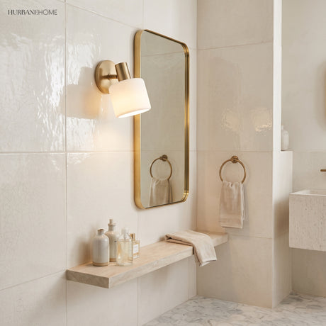 Porcelain shade sconce beside a brass framed mirror in a pale bathroom