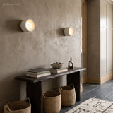 Two compact porcelain disc wall lights on a plaster wall above a bench
