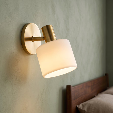 Brass wall sconce with tilted ivory porcelain drum shade on green plaster