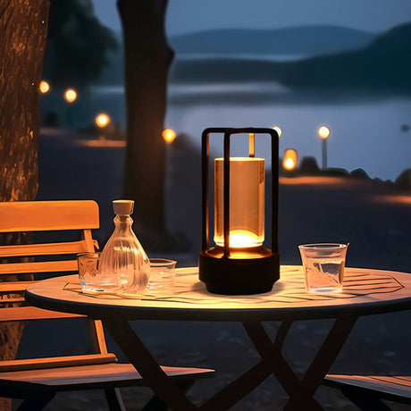 Black cordless lamp on an outdoor table by a lake with string lights behind