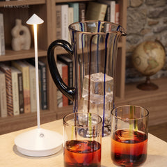 White portable LED table lamp beside a glass jug of iced drink