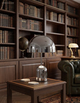 Chrome dome table lamp lit on a side table in a dark panelled library