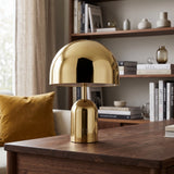 Gold gloss dome table lamp lit on a walnut table in front of a bookshelf