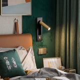 Brass reading sconce on a dark green bedroom wall beside a bed