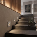 Silver square step light in a plaster wall beside dark treads and slatted timber