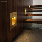 Gold square step light in dark timber panelling lighting a floating stair tread