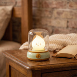 Green based flame night light glowing on a wooden side table beside an open book