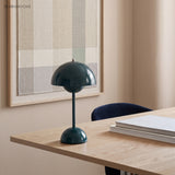 Dark teal rechargeable table lamp on a desk below framed artwork