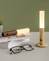 Two cordless wood lamps standing upright on a desk beside reading glasses