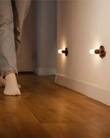 Low mounted light glowing above a wooden floor as someone walks past