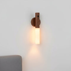 Dark walnut sconce lit on a pale wall above a grey sofa