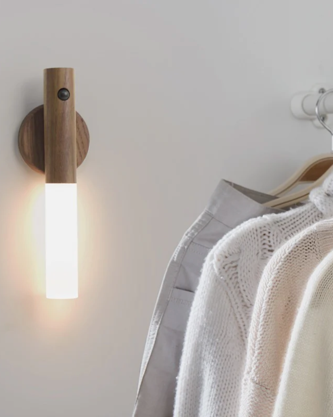 Sconce mounted on a white wall above a rail of hanging knitwear