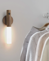 Sconce mounted on a white wall above a rail of hanging knitwear