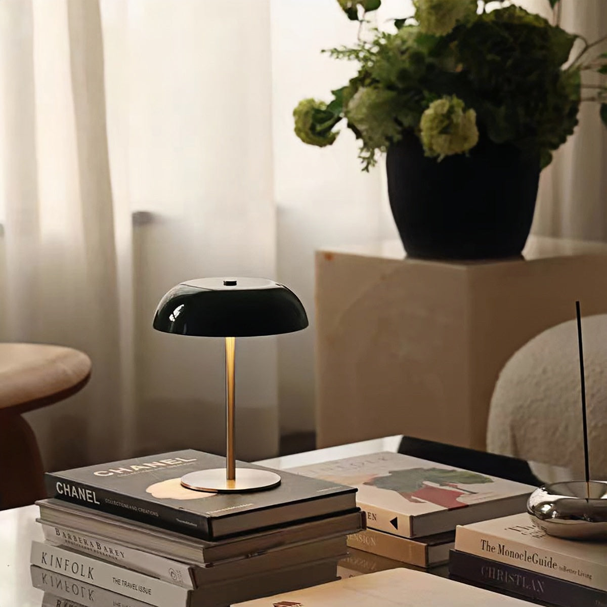 Green dome lamp on books beside a flowering plant by a window