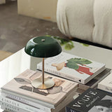 Green dome lamp on a glass coffee table with open magazines