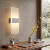 Acrylic panel wall light lit above a desk with books and a vase