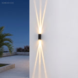 Rectangular wall light throwing crossed beams on a white wall by a palm-lined terrace
