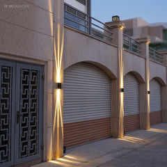 Two black wall lights lighting a beige facade above garage arches at dusk