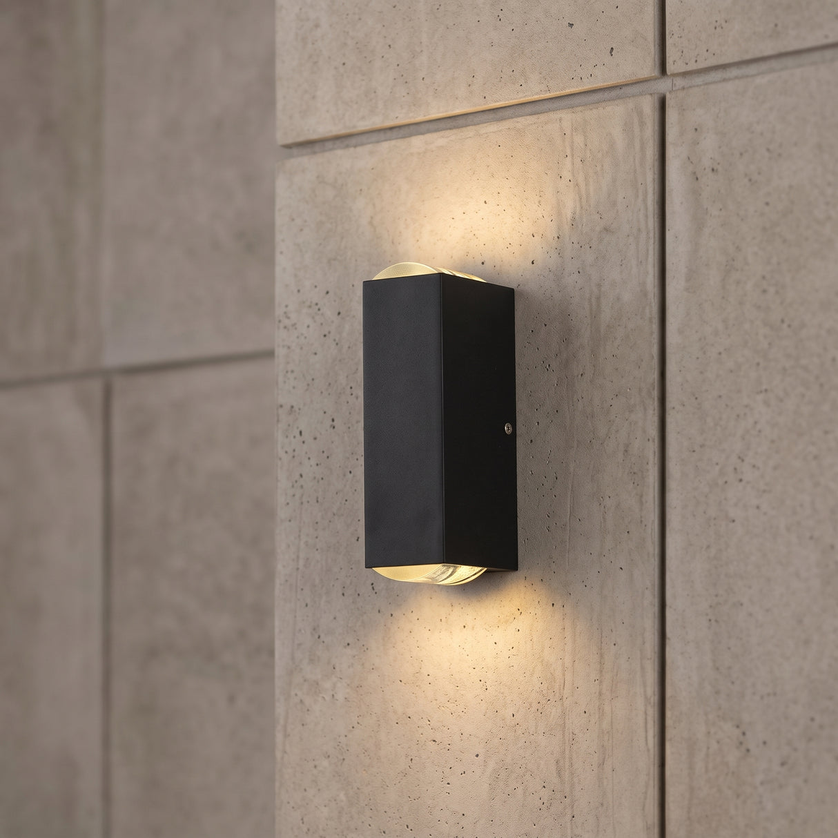 Black rectangular LED wall sconce on a grey concrete tile wall glowing up and down