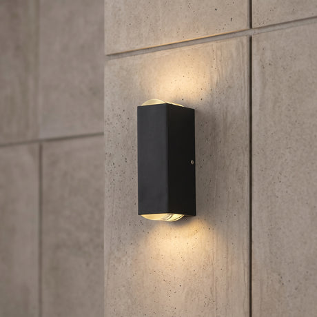 Black rectangular LED wall sconce on a grey concrete tile wall glowing up and down