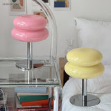 Pink and yellow glass table lamps on a bedside shelf beside a bed