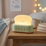 Green retro toaster table lamp glowing warm on a bedside table