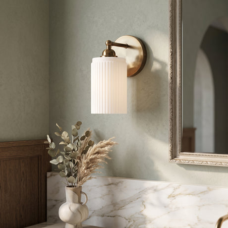 Brass wall sconce with ribbed glass cylinder shade beside a gilt mirror