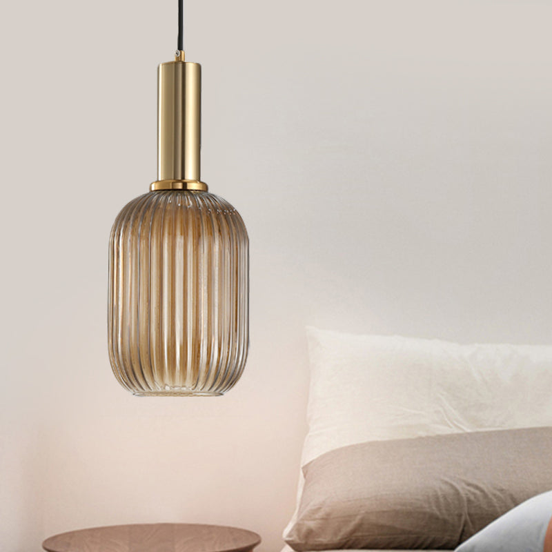 Amber ribbed capsule pendant lit beside a bed in a pink room