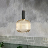 Amber ribbed pendant lit against a wall of green subway tiles