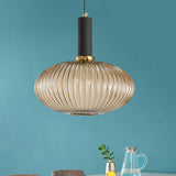 Amber ribbed oval pendant lit against a teal wall above glassware