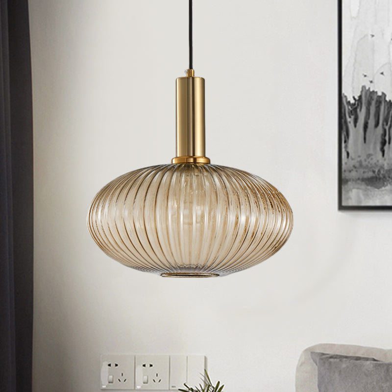 Amber ribbed oval pendant lit on a pale wall beside framed art