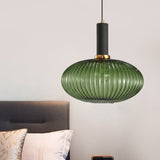 Green ribbed oval pendant lit above a bed with pink cushions