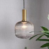 Smoke ribbed pendant lit on a grey wall beside a tall plant