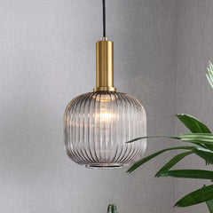 Smoke ribbed pendant lit on a grey wall beside a tall plant