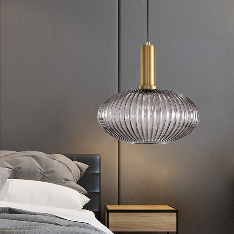 Smoke ribbed pendant lit beside a grey bed and a brass lamp