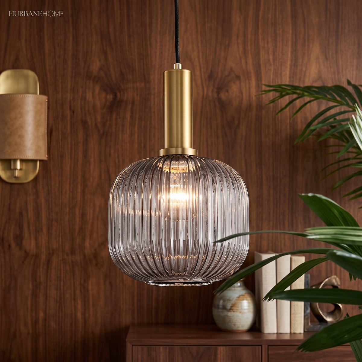 Smoke ribbed oval pendant lit against a walnut wall beside a plant